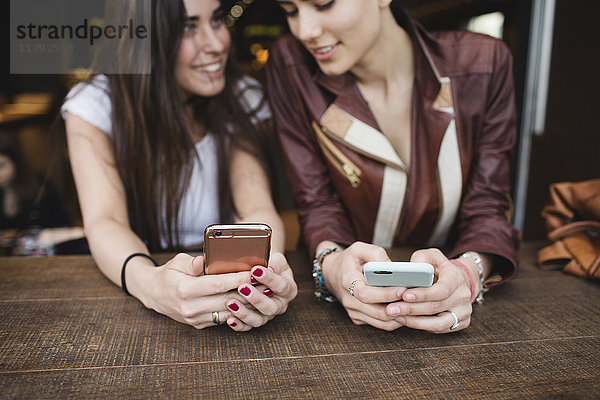 Zwei junge Frauen  die Handys in einer Bar benutzen.