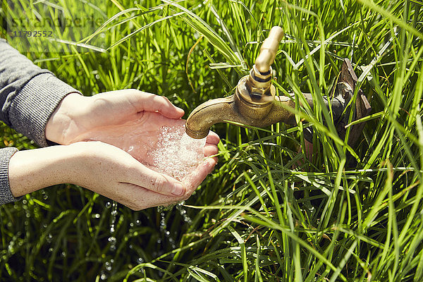 Hände einer jungen Frau trinken Wasser aus einem Brunnen  Nahaufnahme