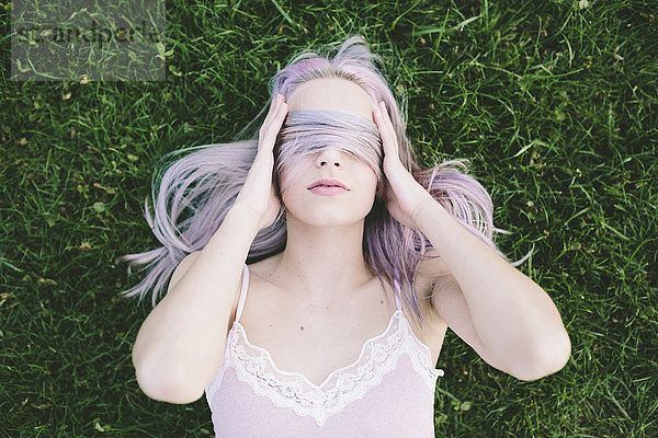 Frau liegt auf Gras und bedeckt die Augen mit ihren Haaren.