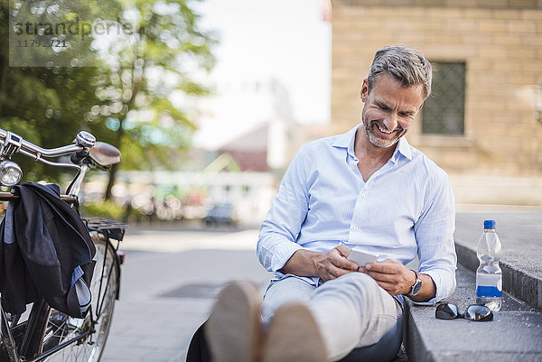 Lächelnder Mann sitzt auf der Treppe in der Stadt mit dem Handy