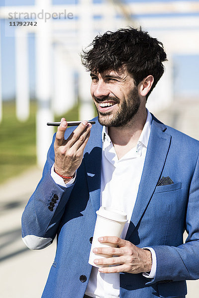 Glücklicher junger Geschäftsmann mit Smartphone und Kaffee zum Mitnehmen im Freien