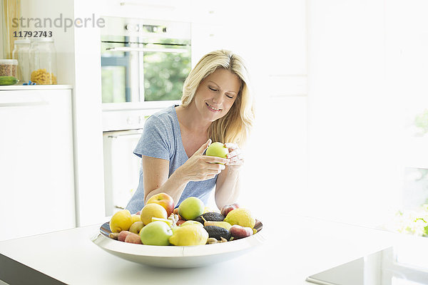Lächelnde Frau zu Hause mit Apfel aus der Obstschale