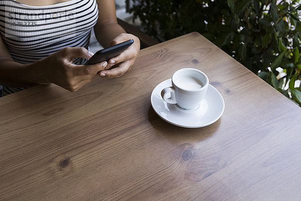 Junge Frau sitzend in einem Café mit Handy  Teilansicht