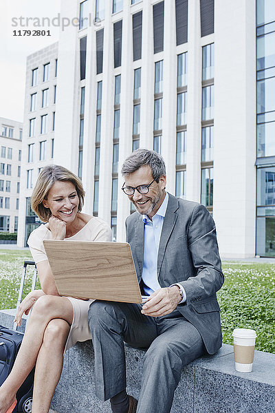 Glückliche Geschäftsfrau und Geschäftsmann teilen Laptop im Freien