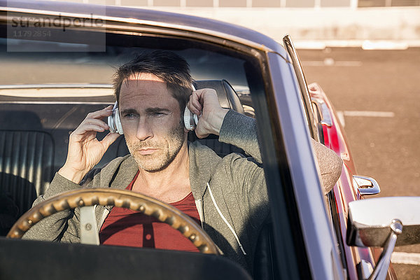 Portrait eines reifen Mannes  der in seinem Sportwagen sitzt und mit Kopfhörern Musik hört.
