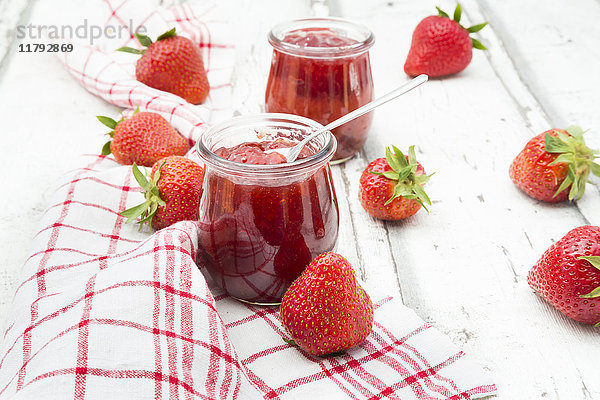 Glas hausgemachte Erdbeermarmelade  Küchentuch und Erdbeeren auf weißem Holz