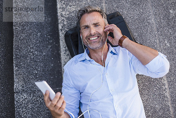 Lächelnder Mann auf der Treppe liegend mit Handy und Ohrstöpseln