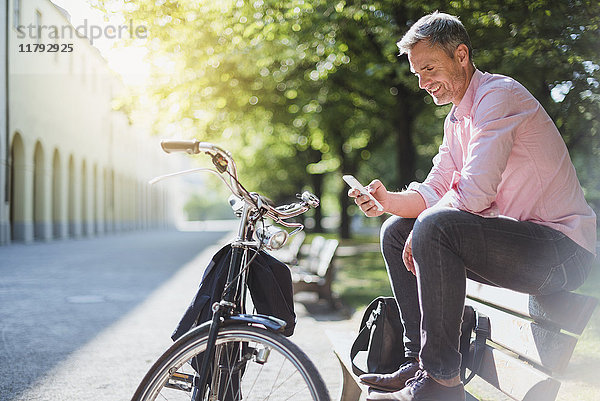 Lächelnder Mann mit Fahrrad beim Telefonieren auf einer Parkbank