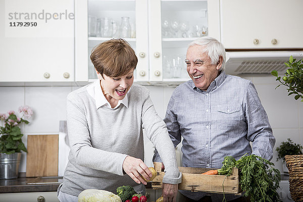 Seniorenpaar steht in der Küche und packt frisches Gemüse aus.