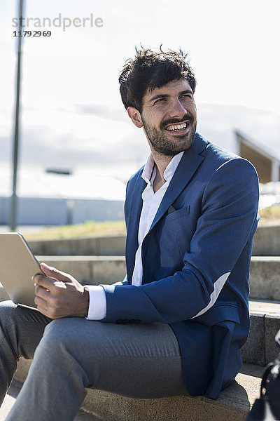 Lächelnder junger Geschäftsmann auf der Treppe sitzend mit umdrehendem Laptop
