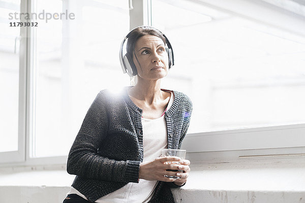 Porträt einer Frau in einem Loft  die Musik mit Kopfhörern hört