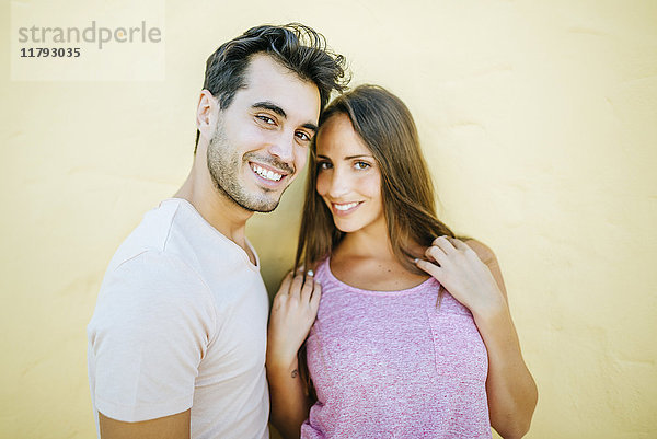 Lächelndes Paar schaut auf die Kamera in der vorderen gelben Wand