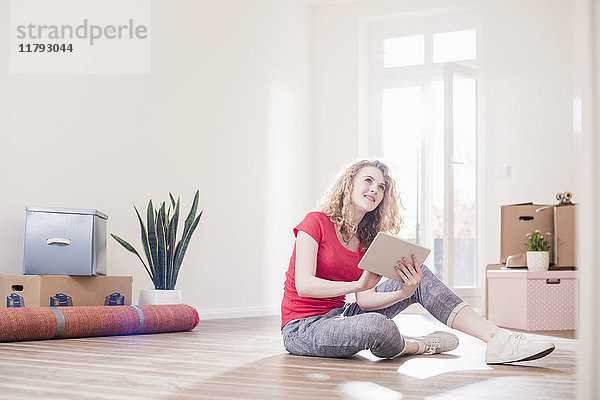 Junge Frau im neuen Zuhause sitzend auf dem Boden mit Tablette