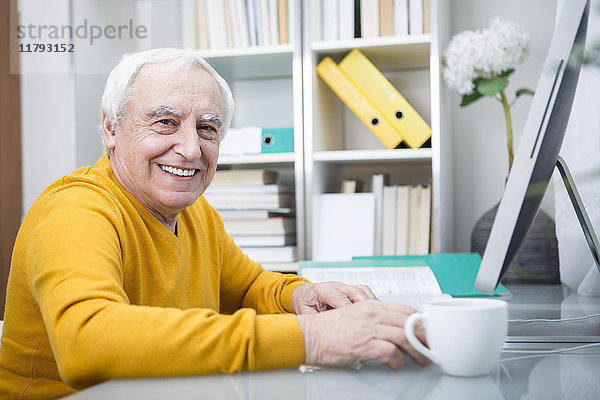 Älterer Mann am Computer bei einer Tasse Kaffee