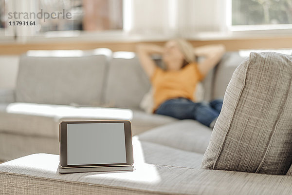 Tablette auf Couch mit entspannter Frau im Hintergrund