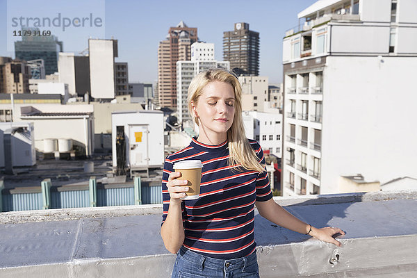Junge Frau trinkt Kaffee auf der Dachterrasse