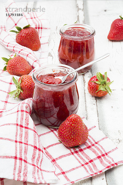 Zwei Gläser hausgemachte Erdbeermarmelade  Küchentuch und Erdbeeren auf weißem Holz