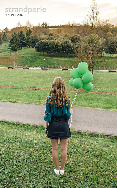 Rückansicht einer jungen Frau mit grünen Luftballons auf einer Wiese stehend