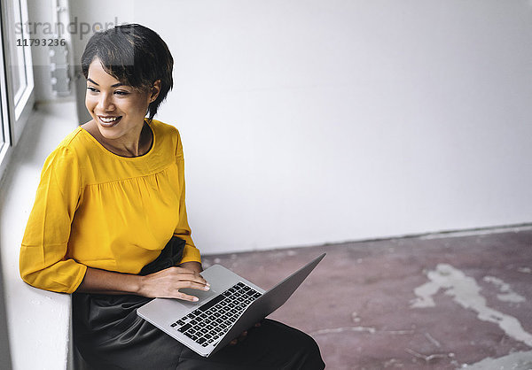 Lächelnde Frau am Fenster sitzend mit Laptop