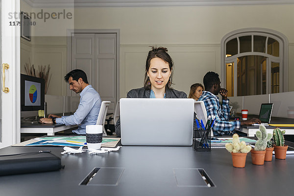 Junge Geschäftsfrau mit Laptop  Kollegen im Hintergrund
