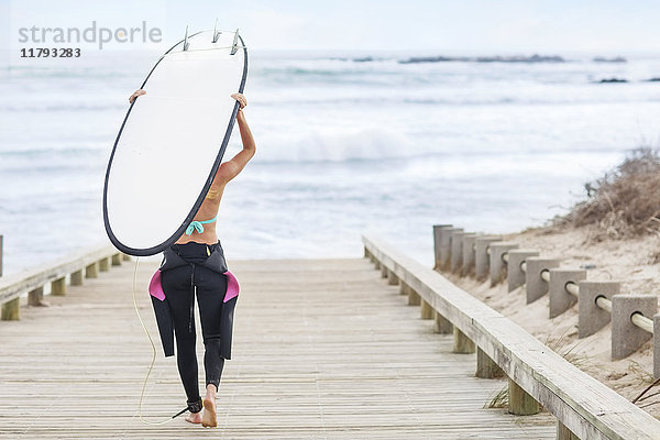 Frau zu Fuß zum Strand mit Surfbrett