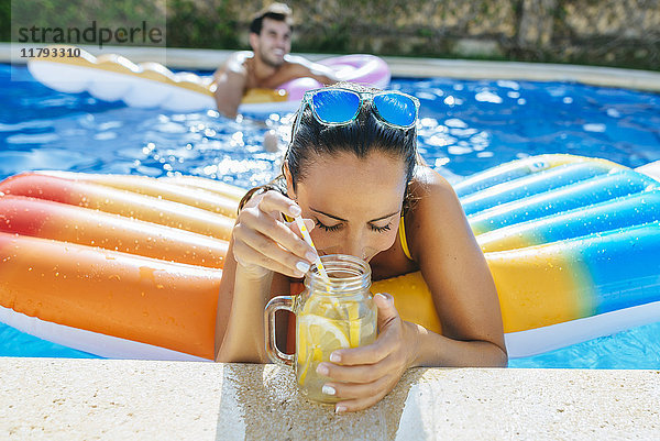Junge Frau im Schwimmbad mit Getränk am Beckenrand