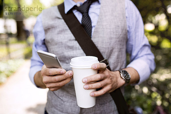 Nahaufnahme eines Geschäftsmannes mit Kaffee und Smartphone im Stadtpark