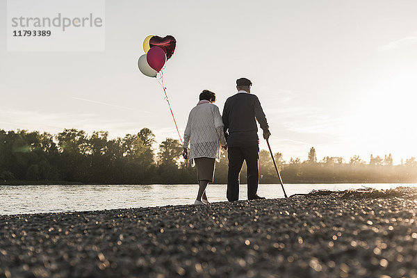 Rückansicht des Seniorenpaares mit Ballons  die abends am Flussufer spazieren gehen.