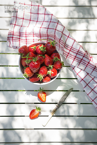 Schale mit Erdbeeren  Messer und Küchentuch auf Gartentisch