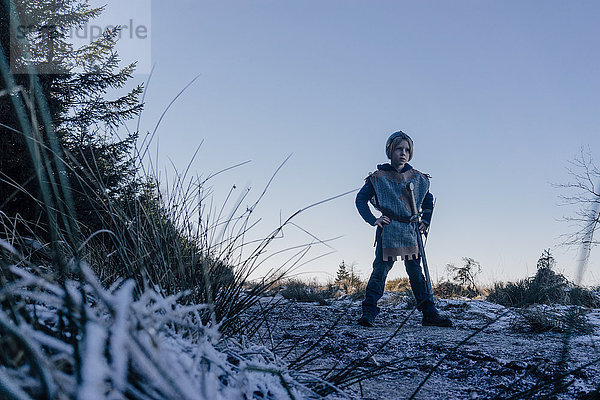 Kleiner Junge  der auf einem Hügel steht und in Ritterkostüm spielt.