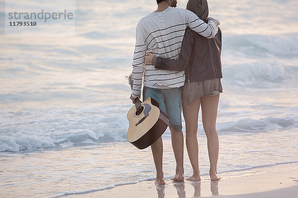 Junges Paar  das mit den Armen auf das Meer blickt.