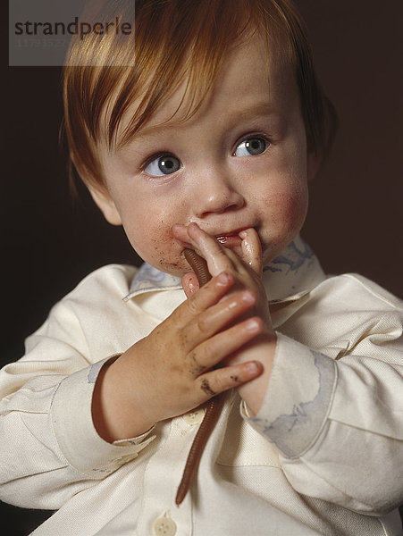 Porträt des rothaarigen Jungen mit Spielzeugwurm und Finger im Mund