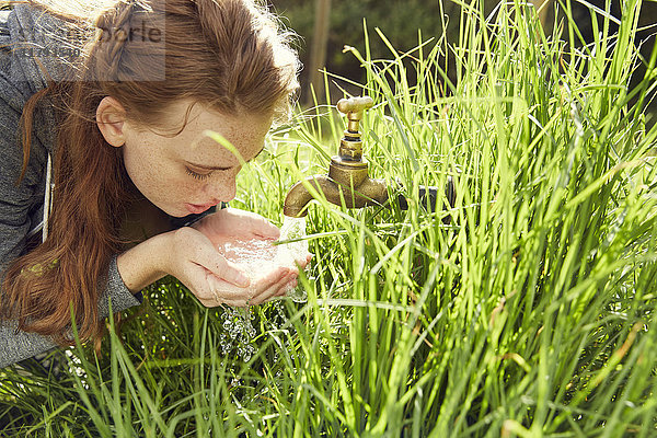 Junge Frau trinkt Wasser aus einem Brunnen