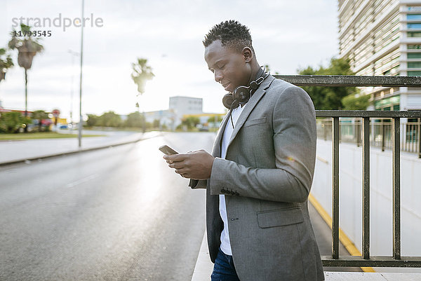 Junger Mann am Straßenrand mit Blick auf das Smartphone
