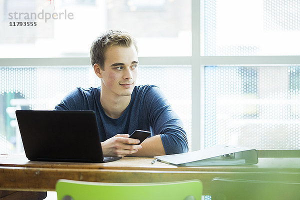 Portrait eines Studenten mit Laptop und Handy im Café