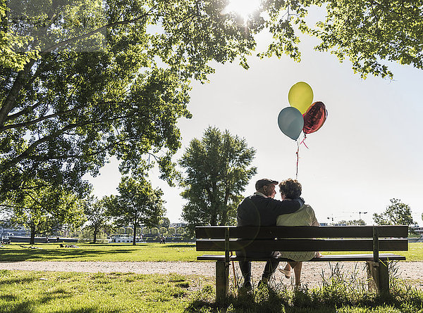 Glückliches Seniorenpaar mit Luftballons auf der Bank im Park