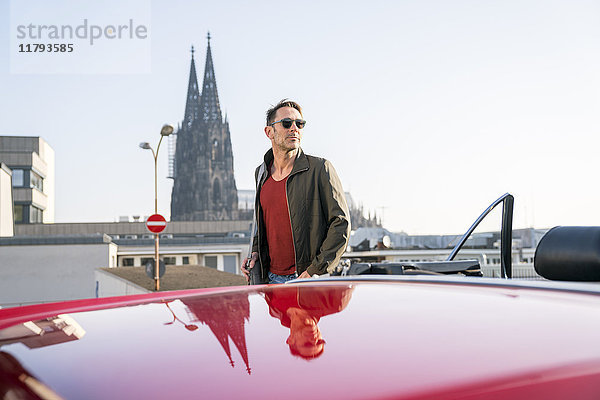 Deutschland  Köln  Portrait eines reifen Mannes  der sich mit seinem geparkten Sportwagen anlehnt.