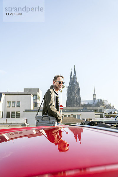 Deutschland  Köln  Porträt eines lächelnden reifen Mannes mit seinem geparkten Sportwagen