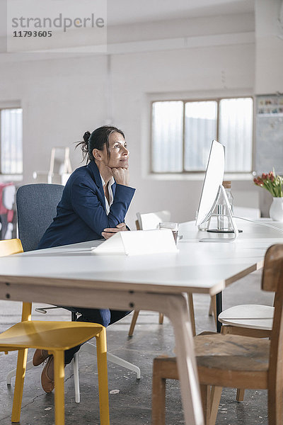 Nachdenkliche Geschäftsfrau sitzt am Schreibtisch in einem Loft