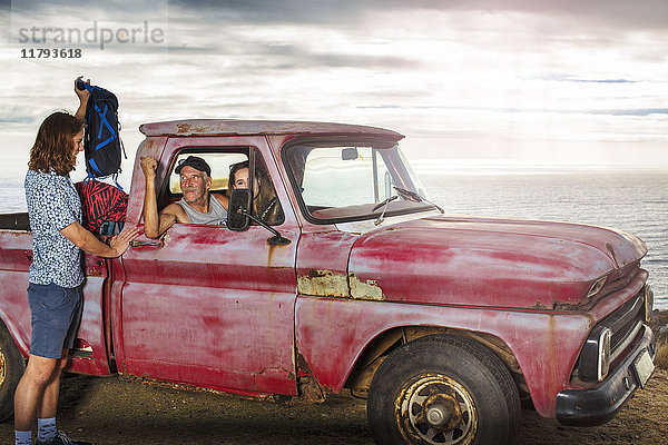 Junger Mann  der seine Sachen von einem alten Pick-Up an der Küste mitnimmt.
