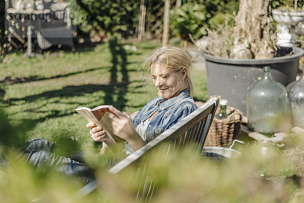 Lächelnde Frau liest Buch auf Gartenbank