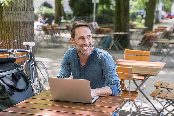 Portrait eines lächelnden reifen Mannes mit Laptop im Biergarten