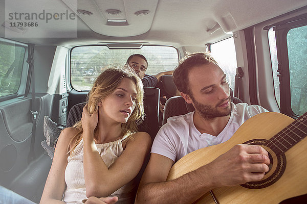 Mann mit Freunden im Auto beim Gitarrespielen