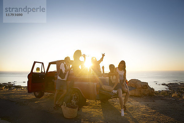 Fröhliche junge Leute draußen holen bei Sonnenuntergang den Lastwagen an der Küste ab.