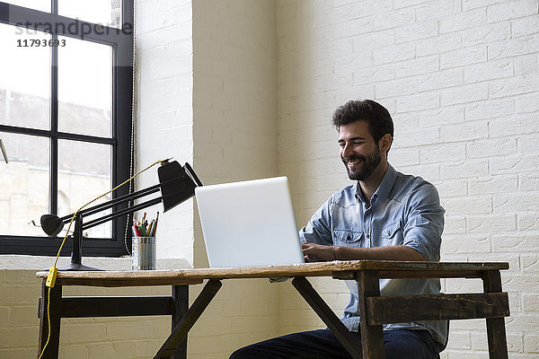 Lächelnder Mann am Schreibtisch mit Laptop