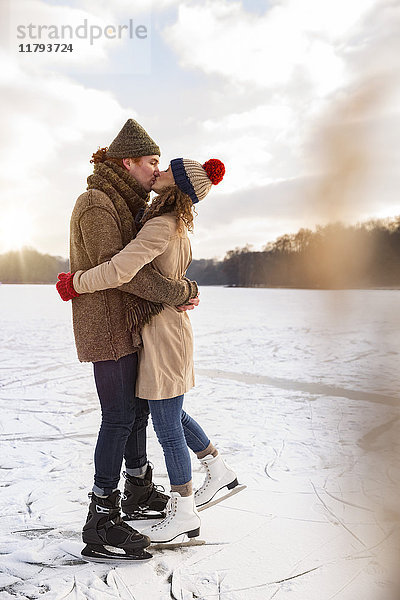 Paar mit Schlittschuhen küssend auf gefrorenem See