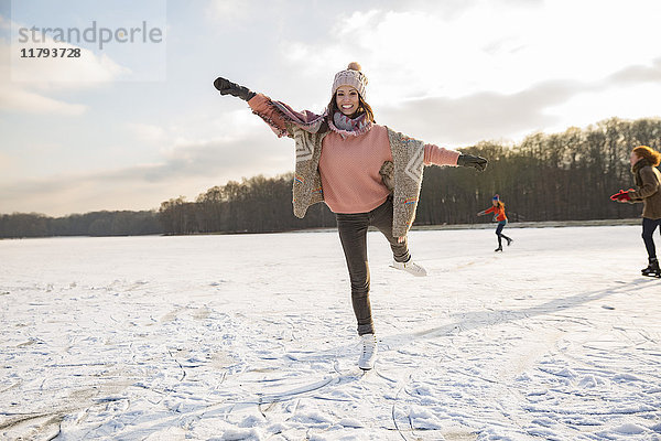 Frau tanzt mit Freunden mit Schlittschuhen auf dem zugefrorenen See