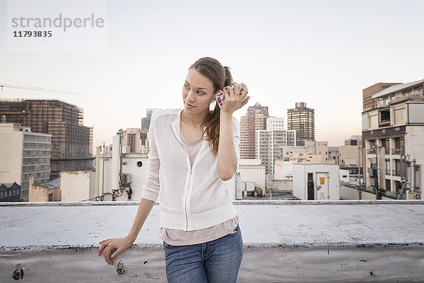 Junge Frau auf einer Dachterrasse stehend  mit Smartphone