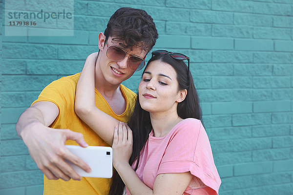Junges Paar nimmt Selfie mit Smartphone vor blauer Ziegelwand