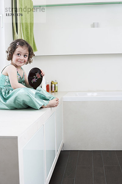 Porträt des lächelnden Mädchens mit Handspiegel im Bad sitzend